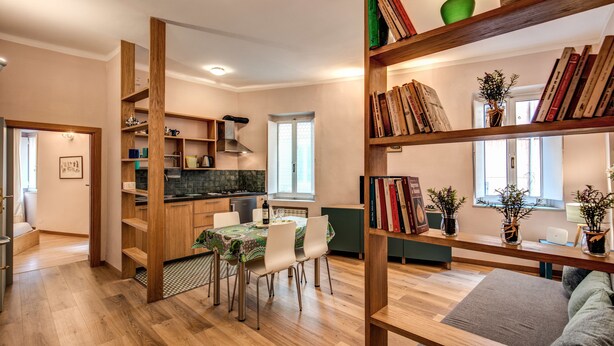 Una cucina moderna con mobili in legno, un tavolo da pranzo con sedie e una libreria piena di libri e piante.