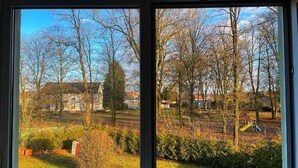 Uitzicht door een raam met heldere lucht, bomen en een speeltuin.