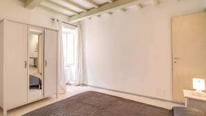 Un dormitorio con un armario grande, una cama con una manta marrón, una mesita de noche con una lámpara y una ventana con cortinas.