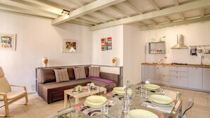 Una sala de estar moderna con un sofá, una mesa de comedor para cuatro personas y una cocina con armarios y una estufa.