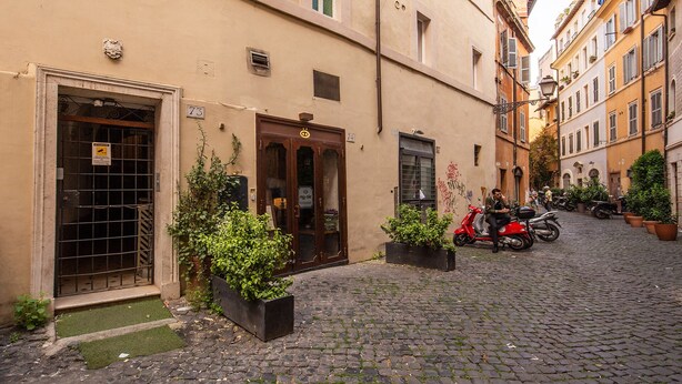 Una calle empedrada con edificios, una scooter roja y plantas en macetas.