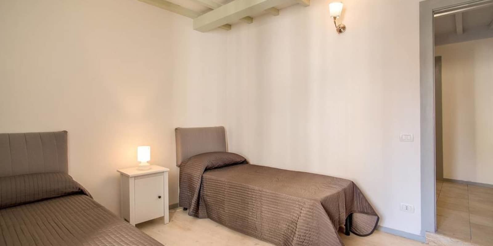 Een kleine, schone kamer met twee eenpersoonsbedden, een nachtkastje en een aan de muur bevestigde lamp.