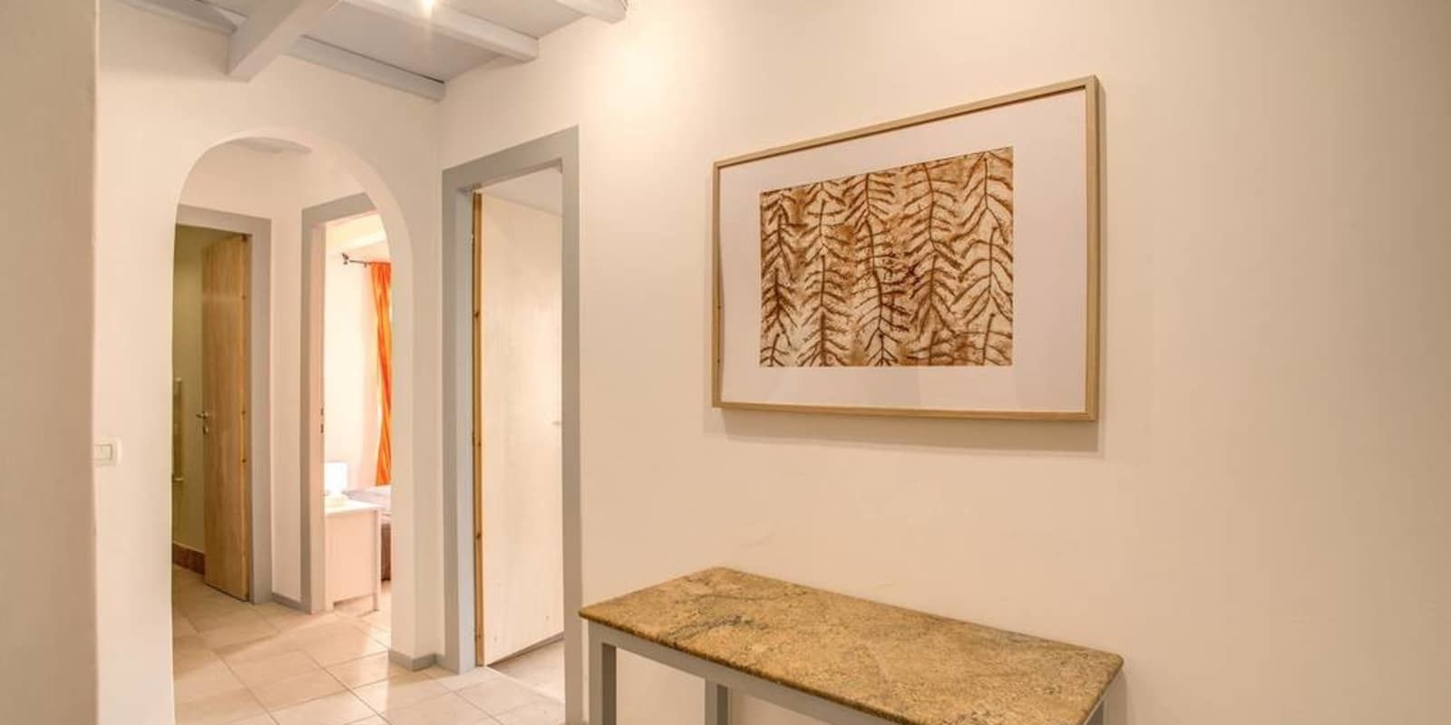 Un passadís amb una obra d'art emmarcada a la paret, una banca i una porta d'arc que condueix a una altra estança.