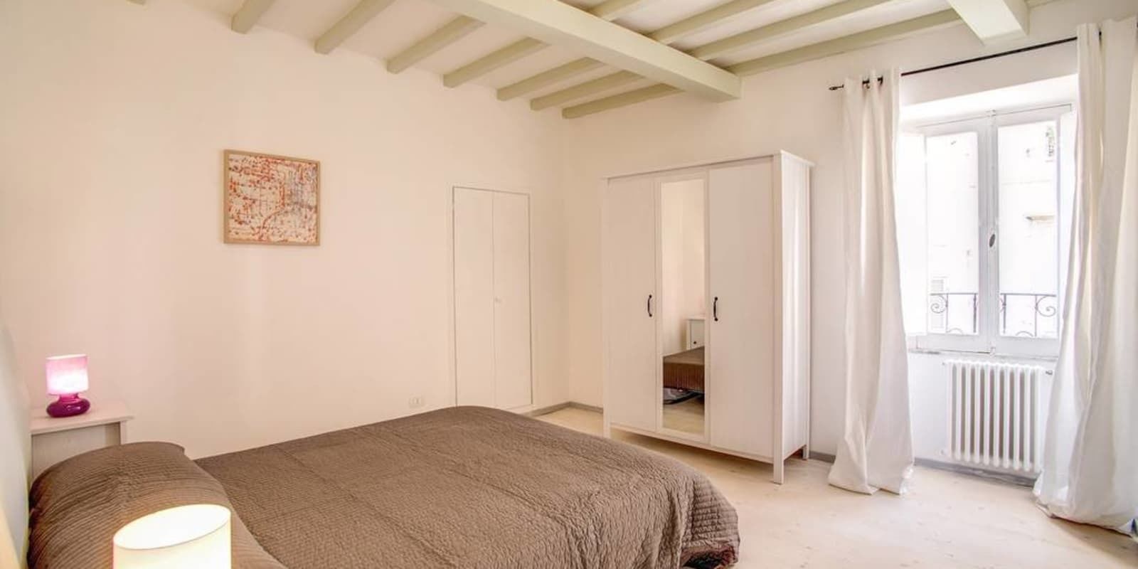 A bedroom with a bed, a bedside lamp, a wardrobe, and a window with curtains.