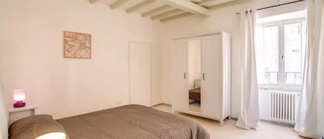 A bedroom with a bed, a bedside lamp, a wardrobe, and a window with curtains.