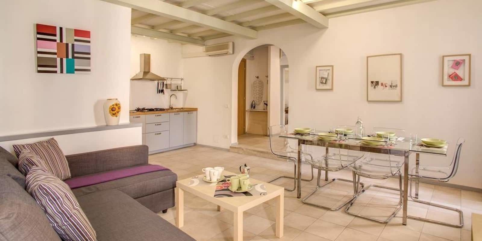 Ein modernes Wohnzimmer mit einer Couch, einem Esstisch mit Stühlen und einer Küche im Hintergrund.