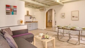 Una sala de estar moderna con un sofá, una mesa de comedor con sillas, y una cocina al fondo.