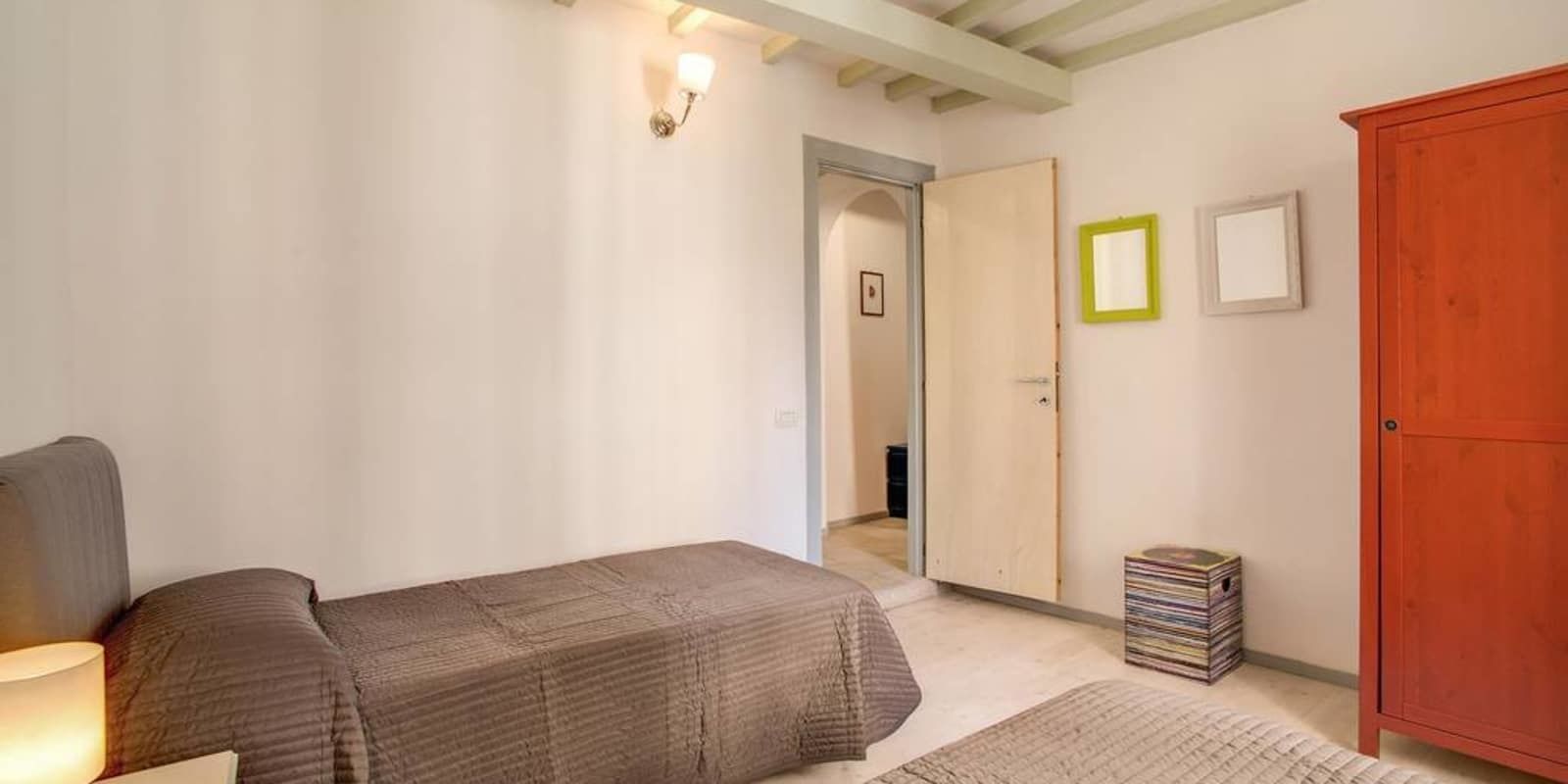 A bedroom with two single beds, a wooden wardrobe, a small bedside table, and a lamp.