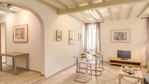 Un amplio salón con una mesa de comedor preparada para cuatro personas, un televisor y un sofá.
