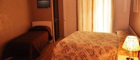 Un dormitorio con cama, mesita de noche con lámpara, televisión en la pared y una puerta.