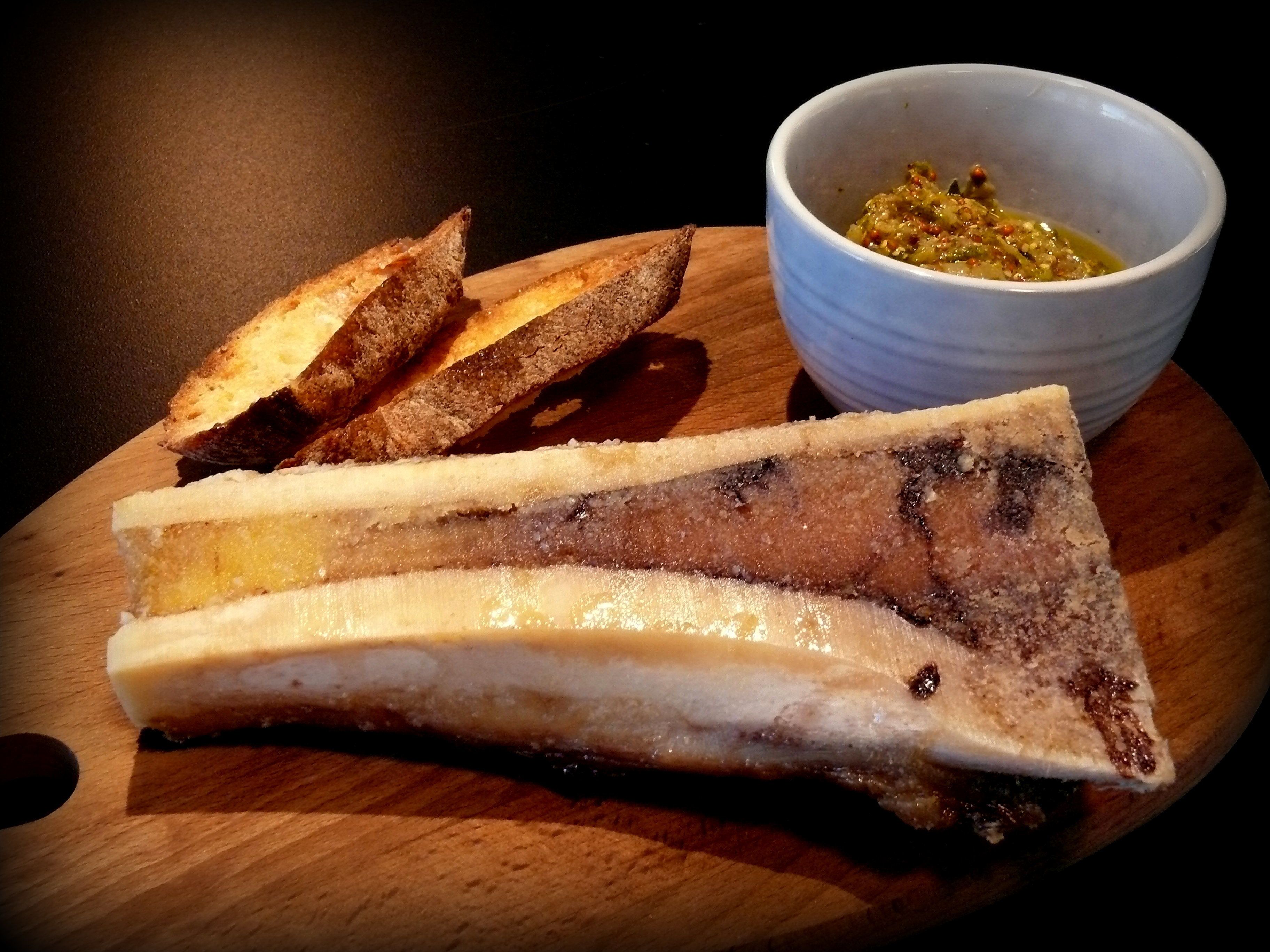 A wooden cutting board with a piece of meat and two slices of bread, and a small bowl of sauce.