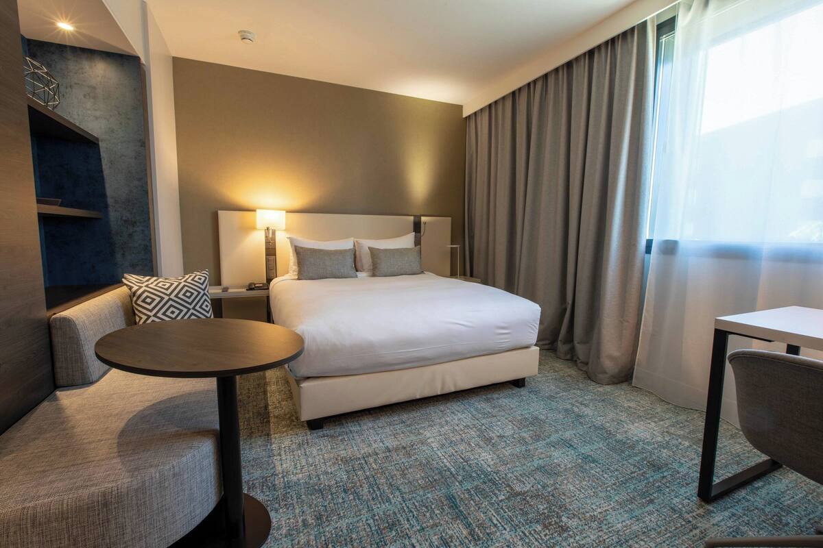 Une chambre d’hôtel moderne avec un grand lit, une petite table ronde, un canapé et un bureau.