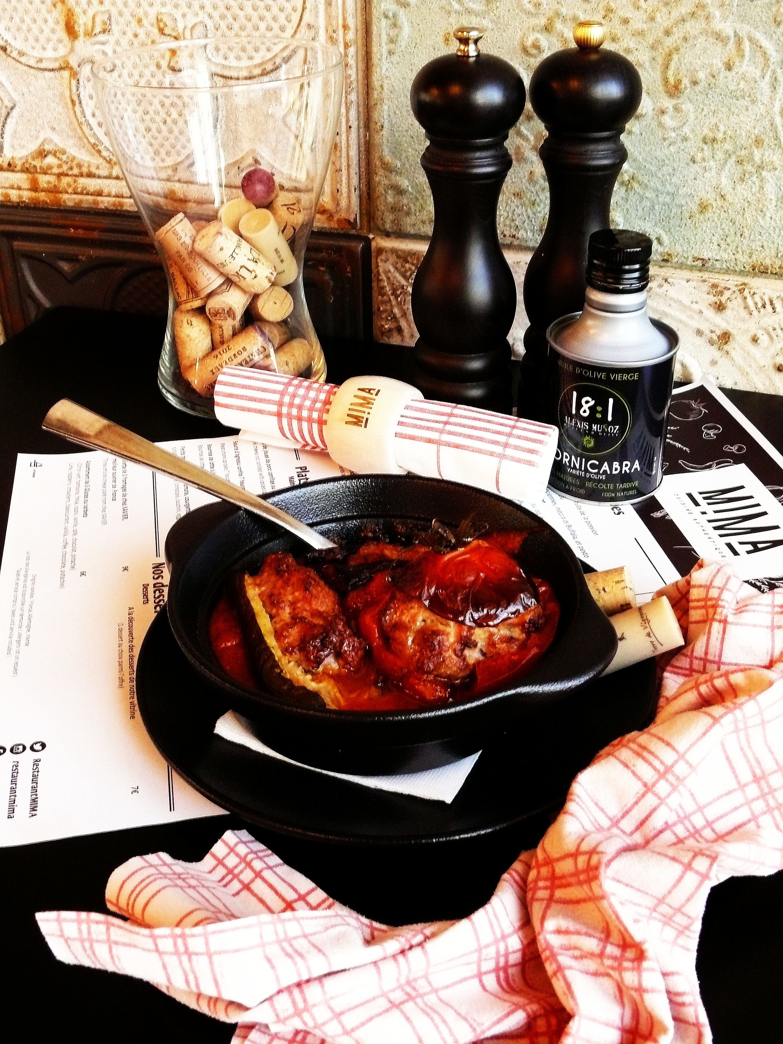 Una mesa de comedor con una sartén negra que contiene comida, una botella de aceite de oliva y un frasco de vidrio con aperitivos.