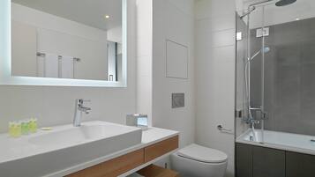 Un baño moderno con un espejo grande, un lavabo blanco, un inodoro y una ducha con mampara de vidrio.