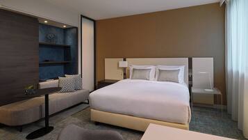 A modern hotel room with a large bed, a sofa, a small table, and a nightstand.