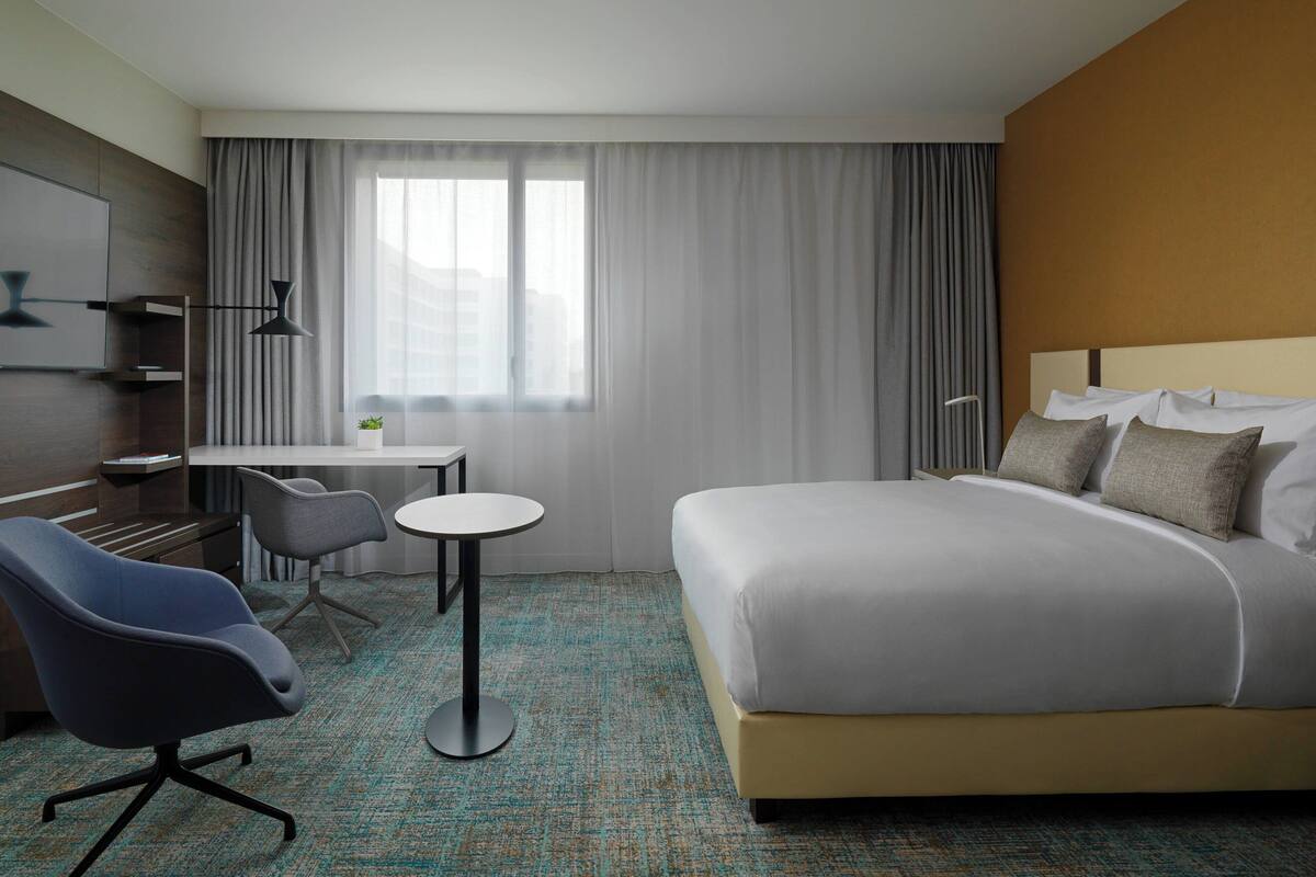 Une chambre d’hôtel avec un lit, un bureau, une chaise et une fenêtre avec des rideaux.