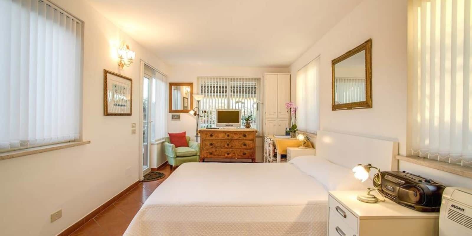 Una habitación de hotel con cama, cómoda, escritorio con lámpara, radio y espejo.