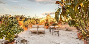 An outdoor patio area with potted plants, a seating arrangement, and a view of a building with a dome. - Exclusive Terrace Largo Argentina (Rome)