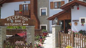 A reception bar and restaurant with a stone facade, wooden shutters, and a balcony with flowers. - Hotel Villa Plinia (Pragelato)