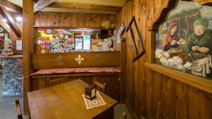 A rustic wooden interior with a bench, a table, and a mural depicting a historical scene. - Hotel Villa Plinia (Pragelato)