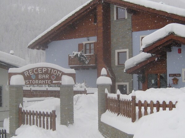 Naamplaat voor receptie, bar en restaurant, houten hekwerk en een gebouw bedekt met sneeuw.