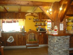 Een rustieke bar met houten balken, een stenen toonbank en planken met flessen.