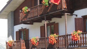 A multi-story building with balconies adorned with flower boxes and a flag. - Hotel Villa Plinia (Pragelato)