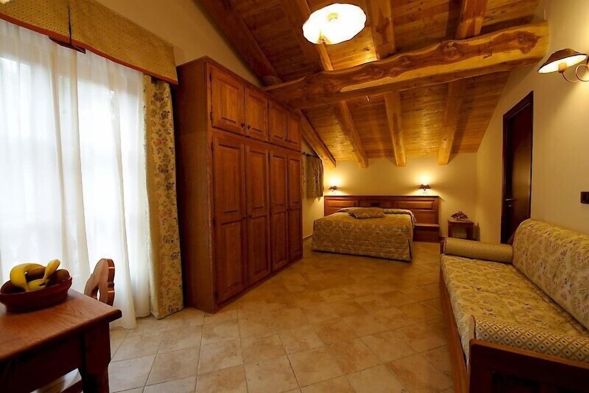 A cozy room with a bed, a sofa, wooden cabinets, and a dining table with a fruit bowl.