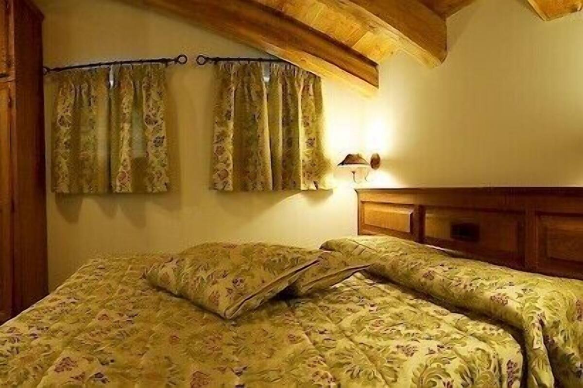 A bedroom with a bed, wooden wardrobe, and a desk with a chair.