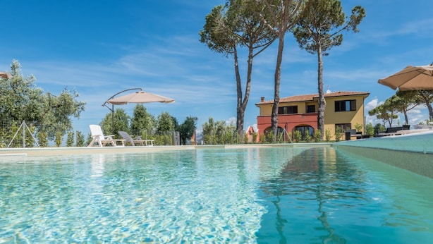 A clear swimming pool with lounge chairs and umbrellas, surrounded by trees and a building with a red roof. - Agriturismo Nonno Gino - Charme&Relax (Piombino)