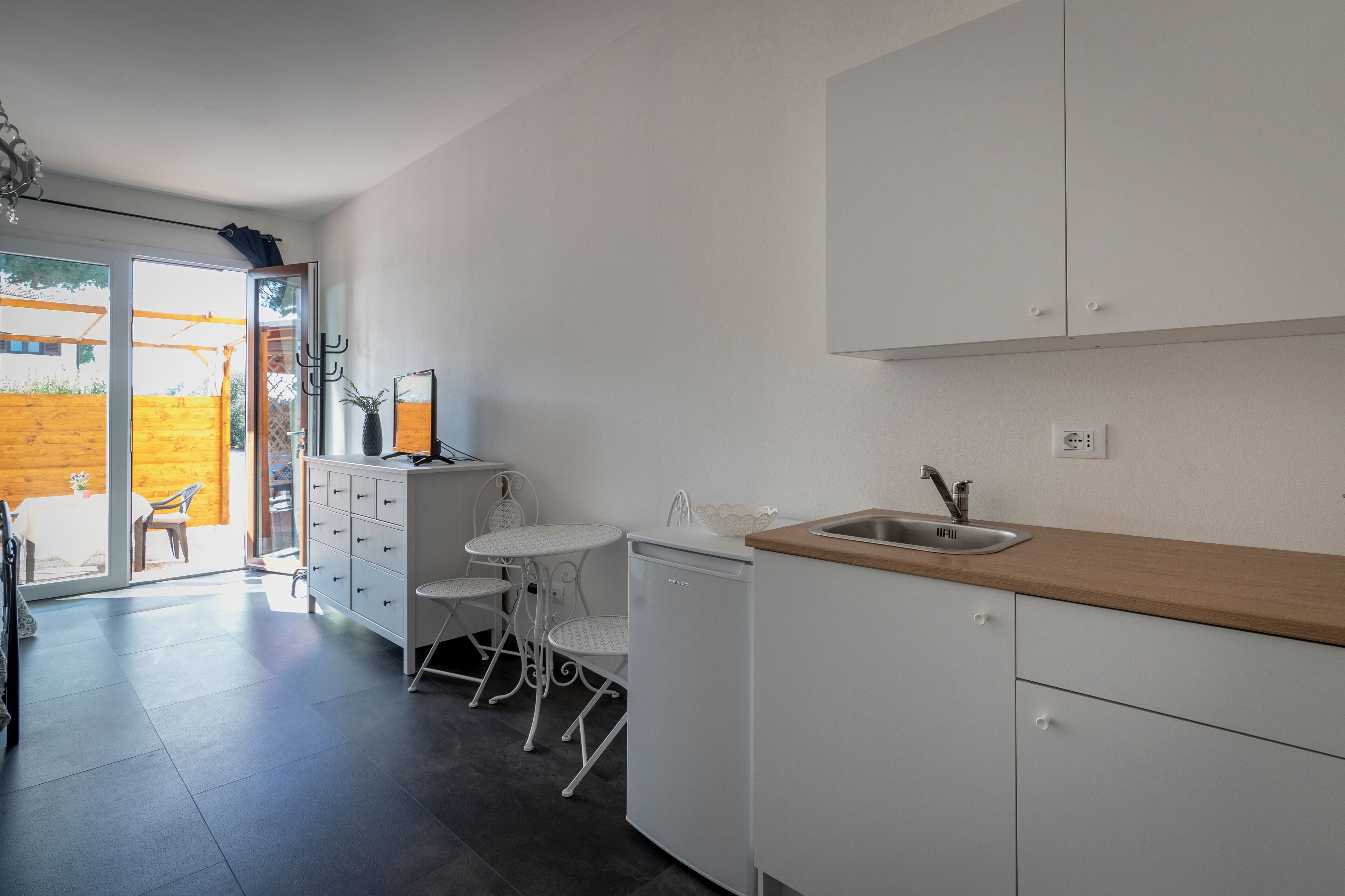 Eine kleine Küche mit weißen Schränken, einer Holz Arbeitsplatte und einem Spülbecken. Es gibt einen kleinen Essbereich mit einem weißen Tisch und Stühlen.