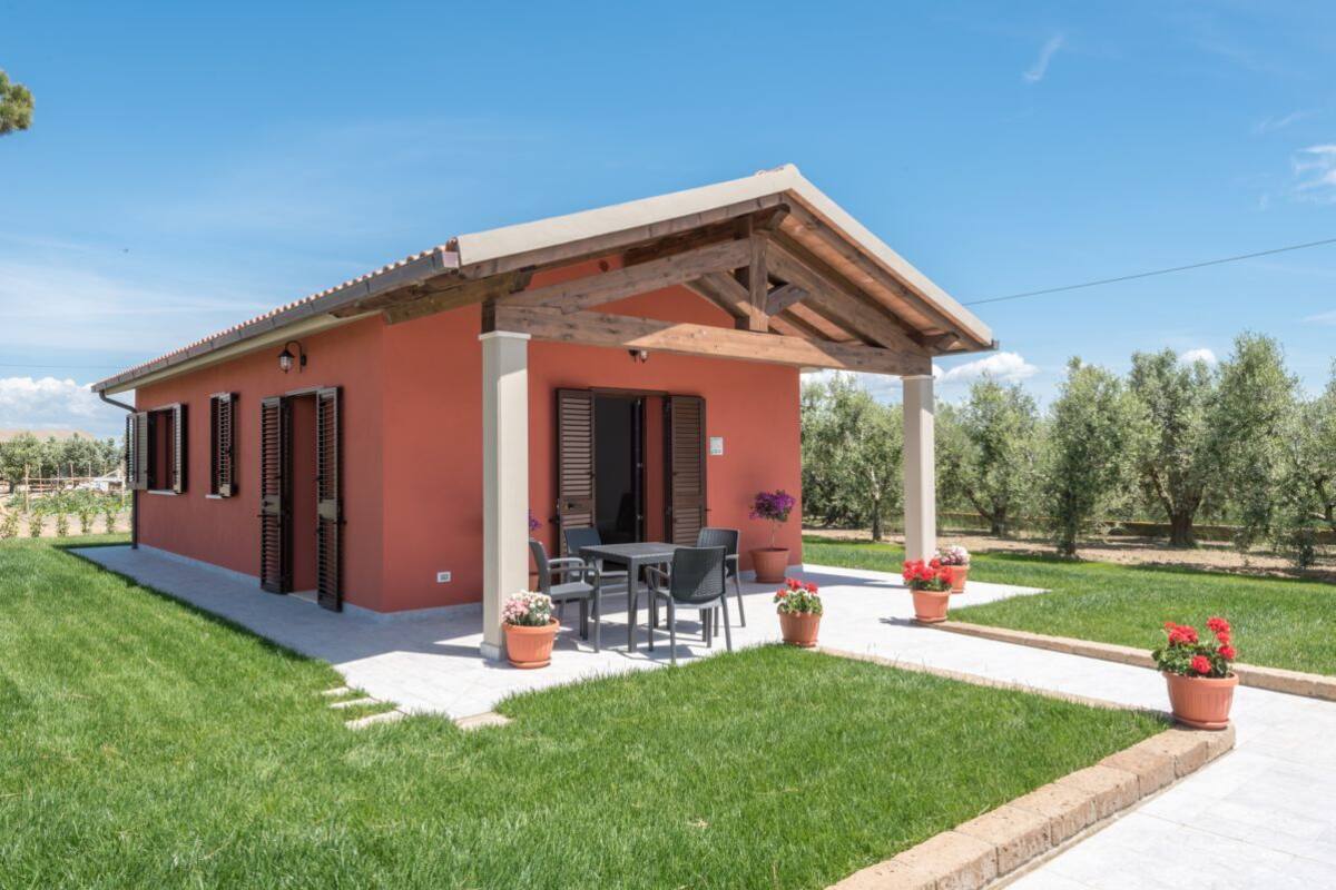 Einbungalow mit überdachter Terrasse, Essbereich mit Tisch und Stühlen sowie Kübelpflanzen.