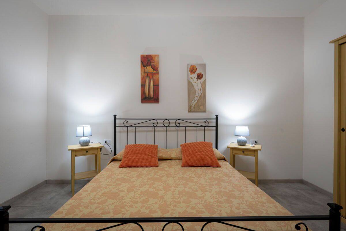 Ein Schlafzimmer mit einem Bett, zwei Nachttischen, zwei Lampen, zwei orangefarbenen Kissen und zwei Wandbildern.