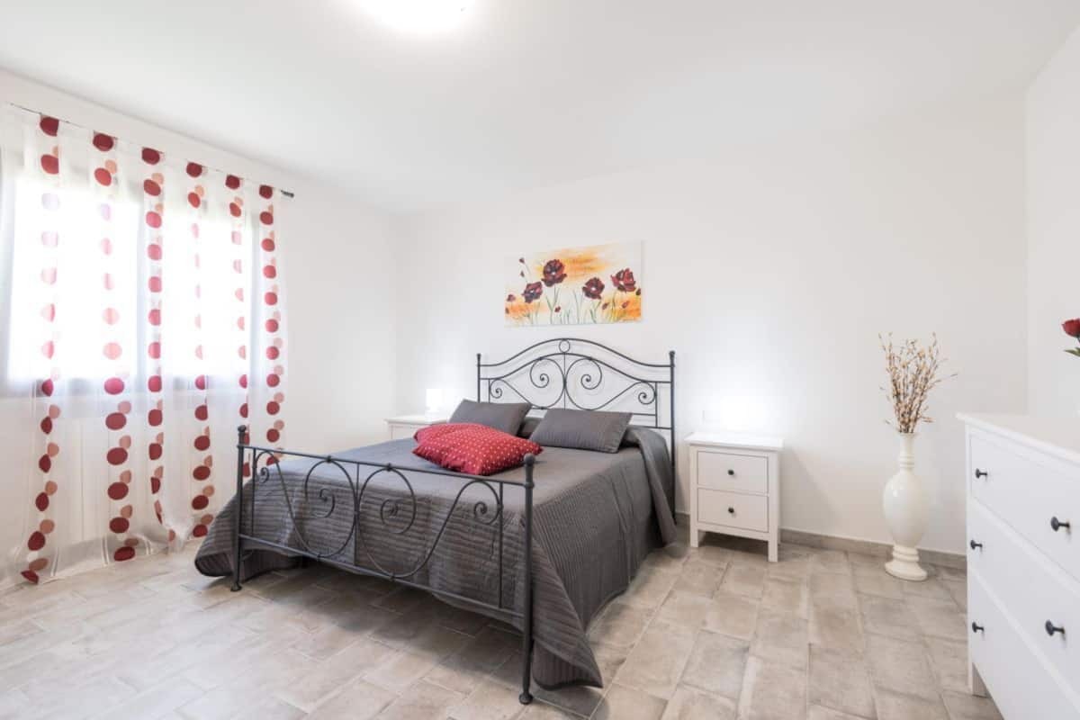 Ein Schlafzimmer mit Bett, Nachttisch, Schminktisch und einem Bild an der Wand sowie einem Fenster mit Vorhängen.