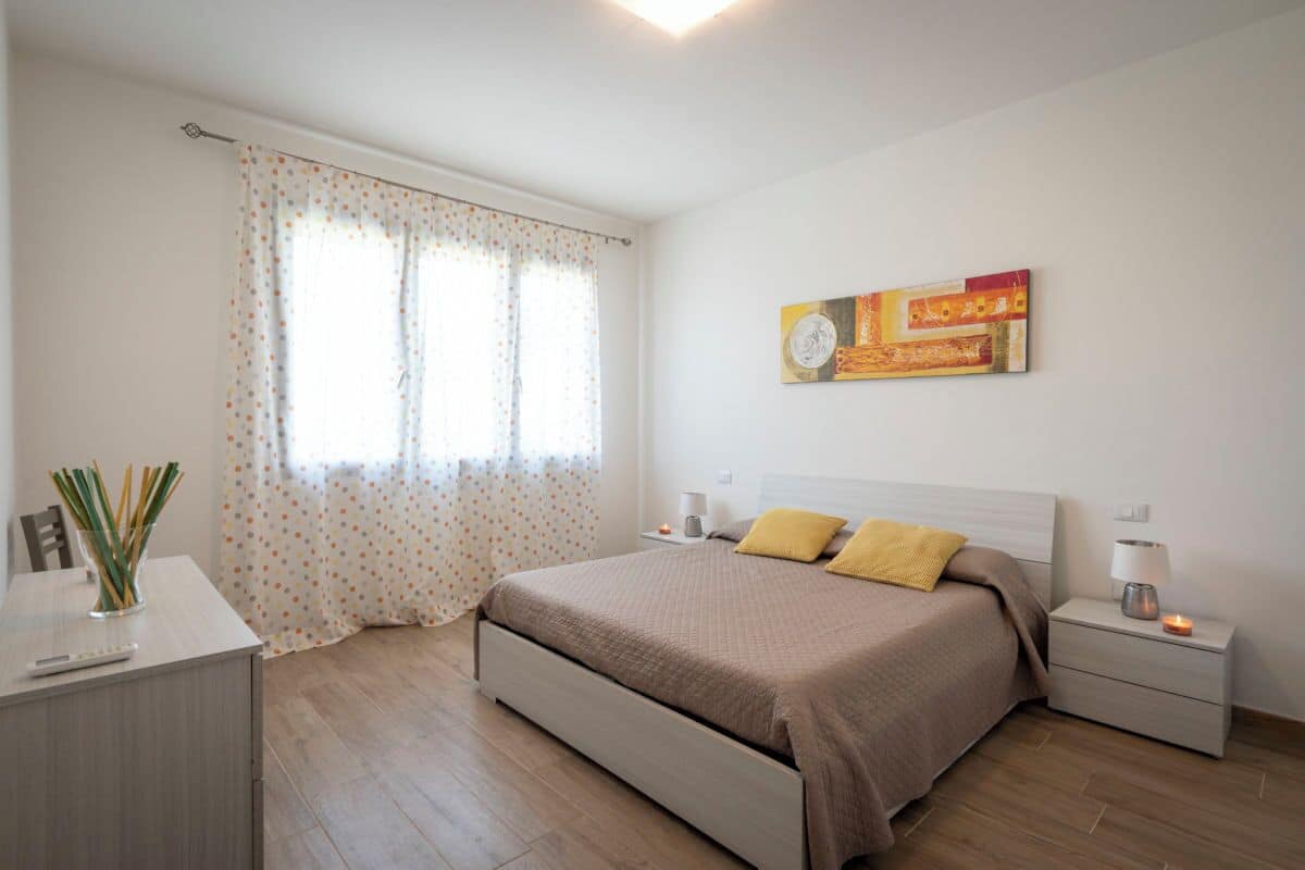 Ein Schlafzimmer mit Bett, Nachttischen, einer Lampe, einem Bild und einem Vorhang.
