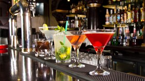 A bar with a variety of drinks, including cocktails and a non-alcoholic beverage, with a background of shelves stocked with bottles. - Exclusive One Bedroom Suite (Boston)
