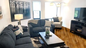 A living room with a sofa, armchair, coffee table, and a TV stand. - Exclusive One Bedroom Suite (Boston)