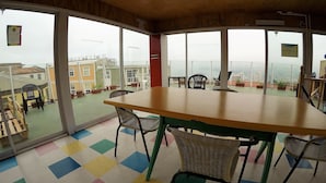 Una habitación con una mesa grande y sillas, ventanas amplias con vistas a edificios, y un suelo de colores.