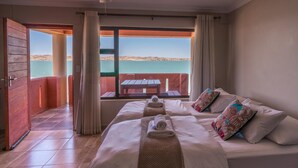 A hotel room with two beds, a view of the sea, and a balcony with a table and chairs. - Island Cottage Guesthouse (Luderitz)