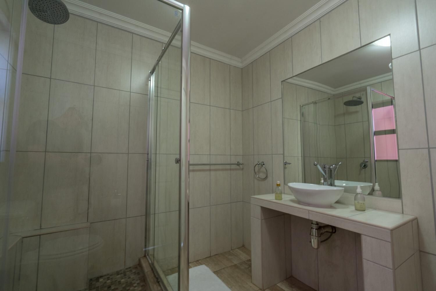 A modern bathroom with a glass-enclosed shower, a white sink, and a large mirror.