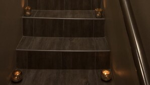 A staircase with dark wooden steps, a metal handrail, and two framed pictures on the wall. - Island Cottage Guesthouse (Luderitz)