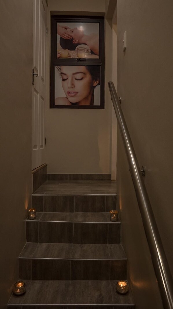 Un escalier avec une rampe métallique, des marches en bois foncé et deux tableaux encadrés accrochés au mur.