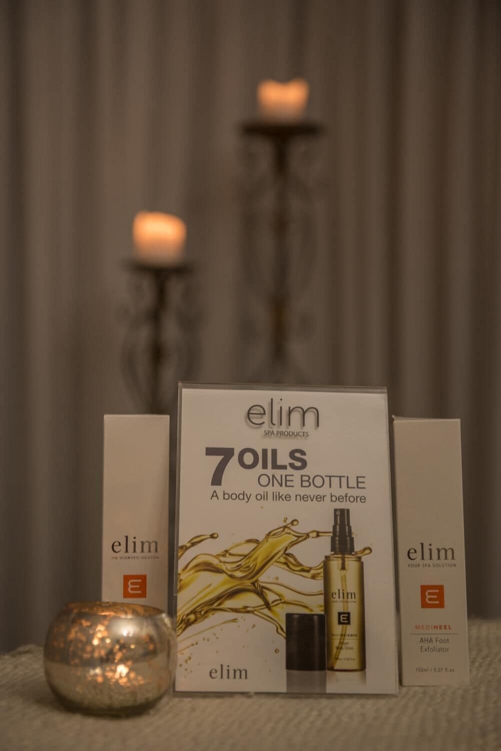 A display of Elim spa products, including a box labeled "7 Oils One Bottle" and a bottle of Elim AHA Foot Exfoliator.