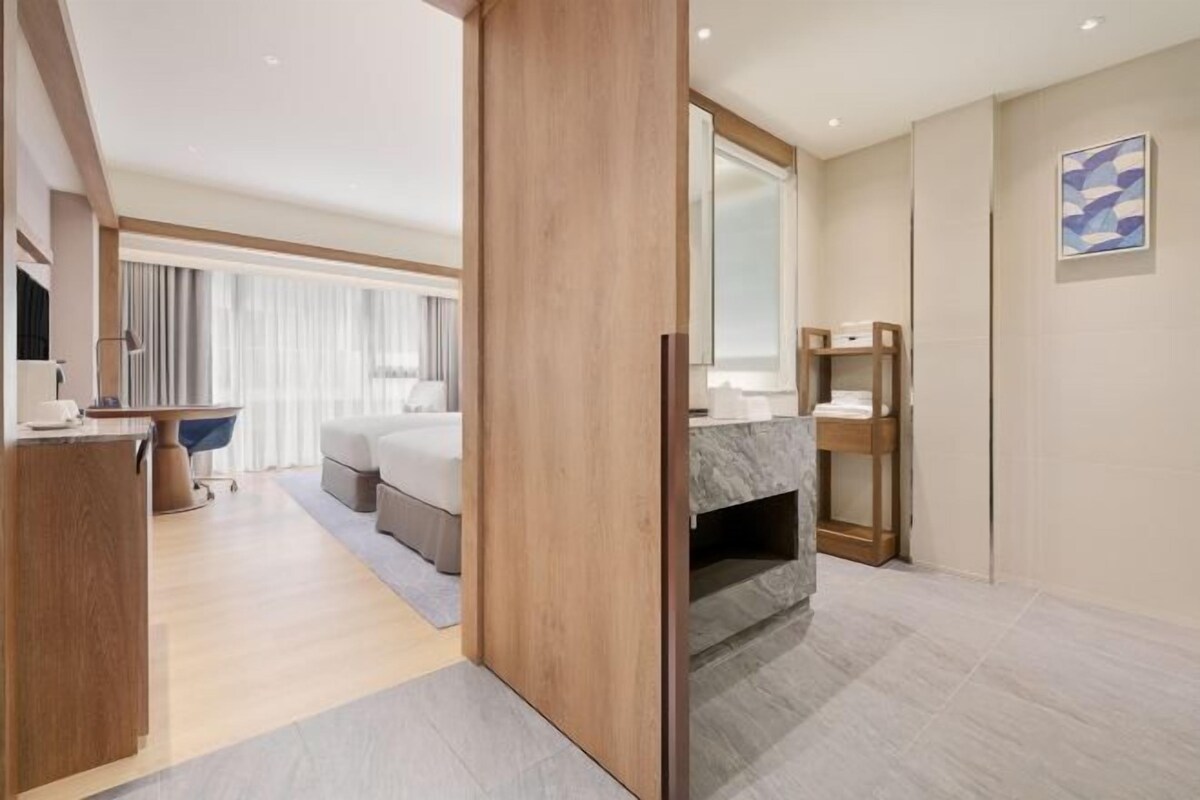 A modern hotel room with a wooden partition, a bed, a desk, and a bathroom with a marble vanity.