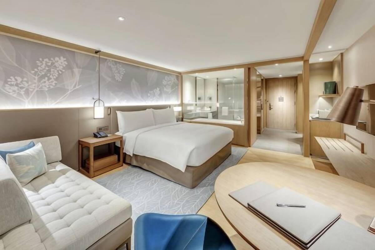 A modern hotel room with a large bed, a sofa, a desk, and a mirror.