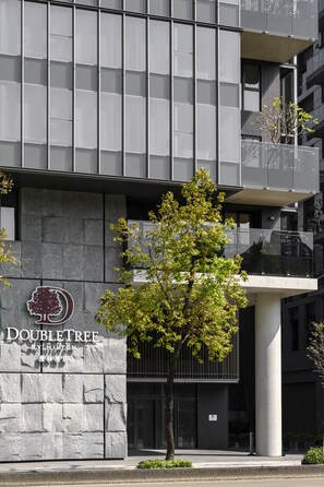 A DoubleTree hotel with a modern facade, a prominent tree in front, and a clear view of the entrance. - DoubleTree by Hilton Taipei Zhongshan (Taipei)