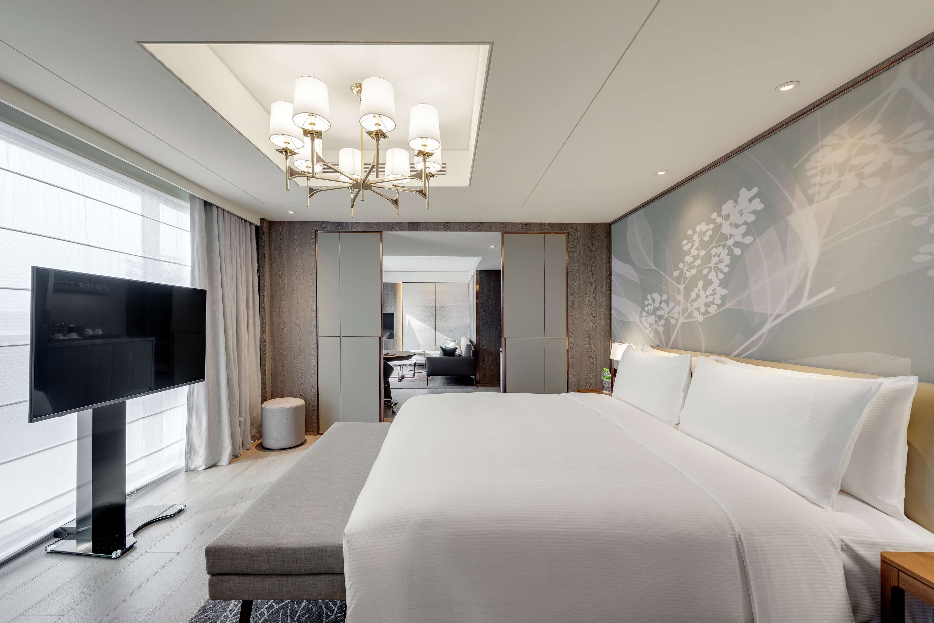Une chambre d’hôtel moderne dotée d’un grand lit, d’un téléviseur à écran plat, d  ’un lustre et d’un mur décoratif.