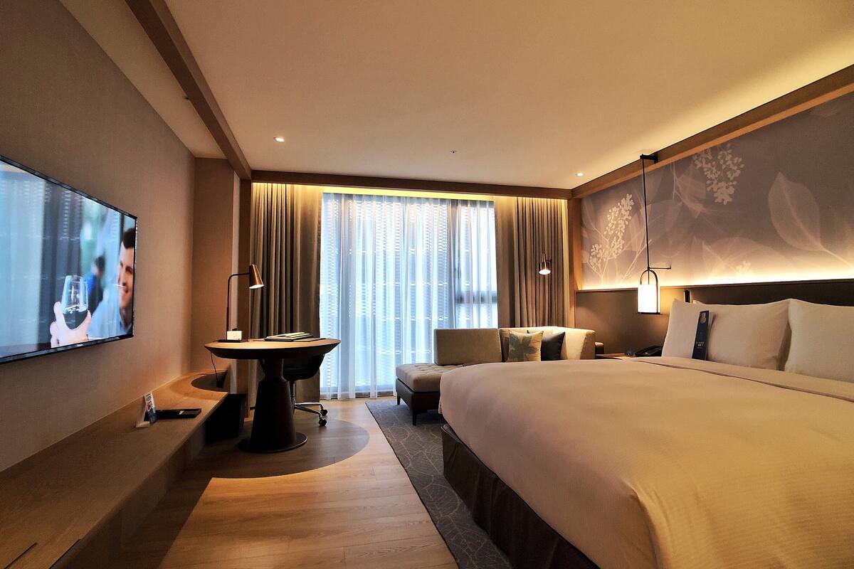 A hotel room with a large bed, a desk with a chair, a television, and a window with curtains.