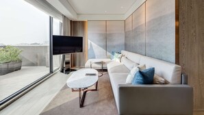 A modern living room with a large flat-screen TV, a sofa, a coffee table, and a view of the city through large windows. - DoubleTree by Hilton Taipei Zhongshan (Taipei)