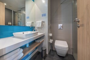 A modern bathroom with a white sink, a mirror, a shower, and a toilet.